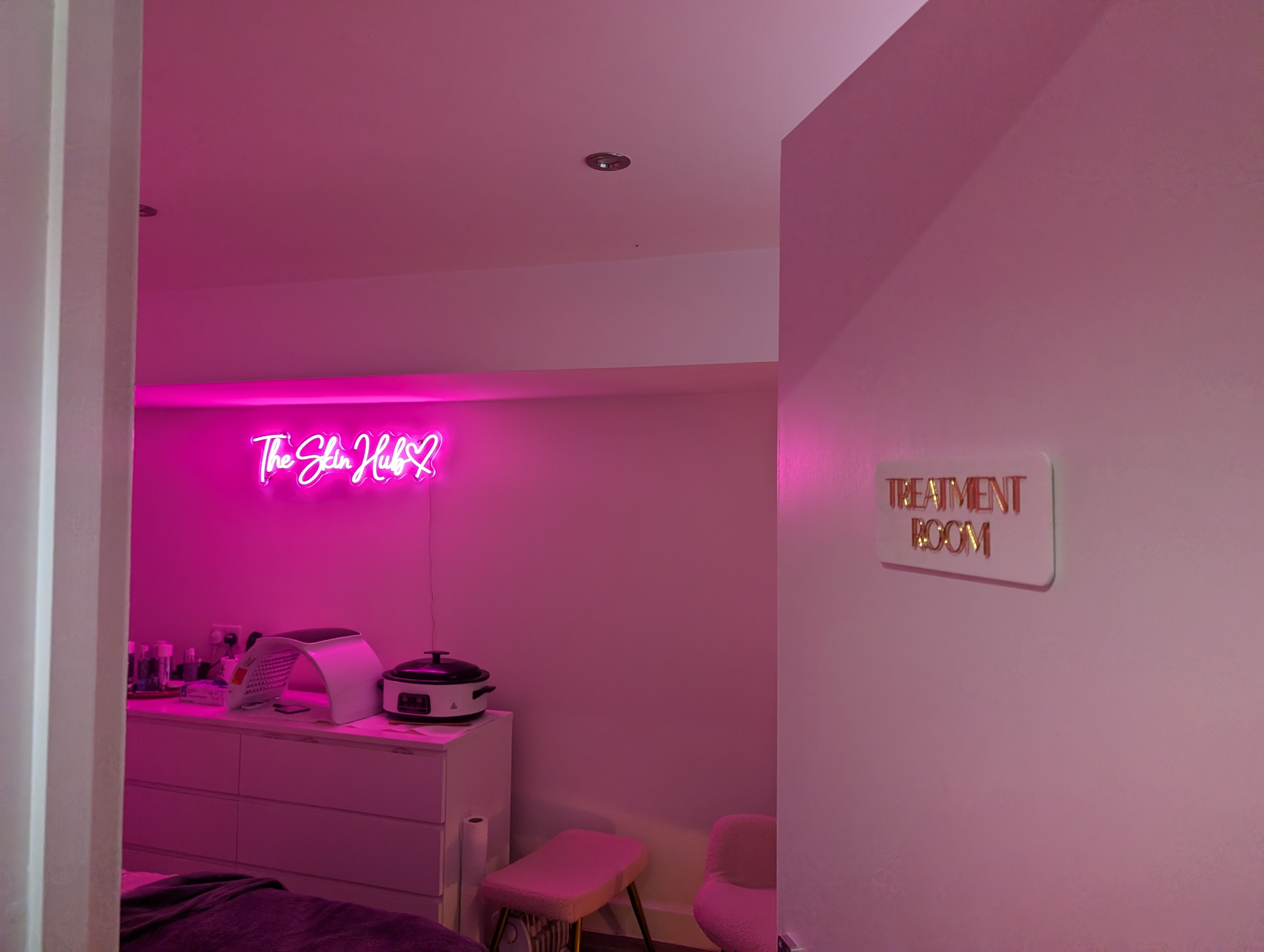 Entrance door with gold Treatment Room plaque looking into The Skin Hub neon