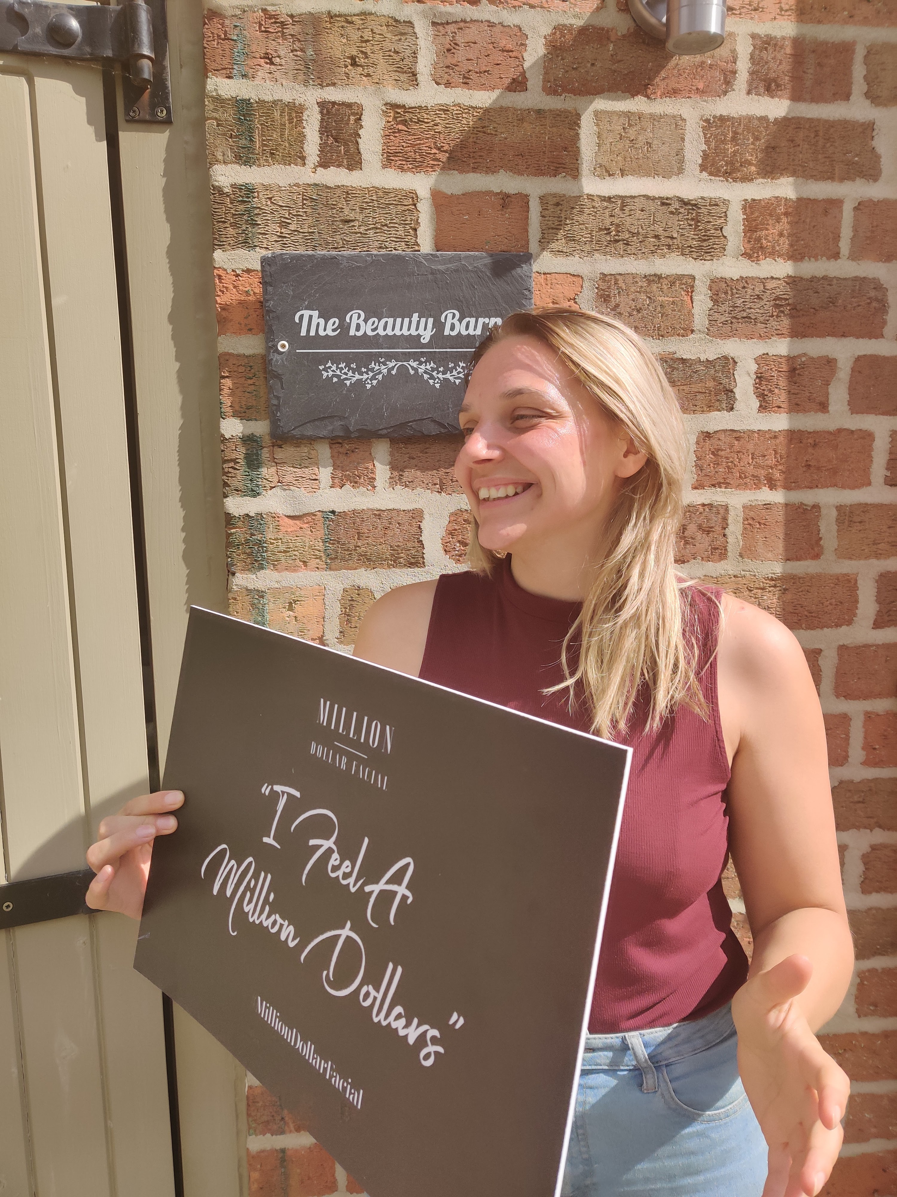 Smiling client holding I Feel A Million Dollars sign outside The Beauty Barn